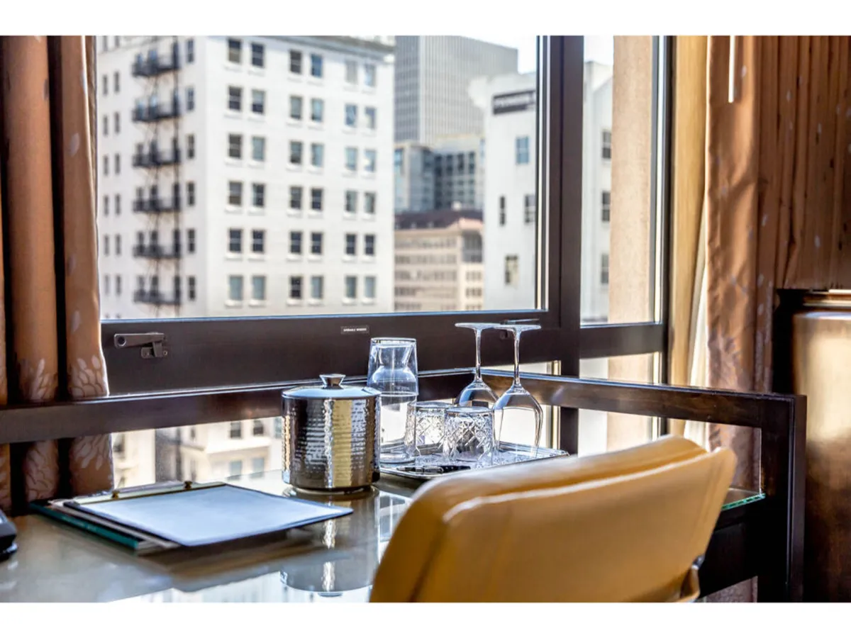 A cozy table and chair are positioned next to a large window, offering a panoramic view of the city below. The elegant setting is perfect for enjoying a morning coffee, reading, or working while soaking in the urban landscape. Decorative elements and soft lighting enhance the tranquil atmosphere.