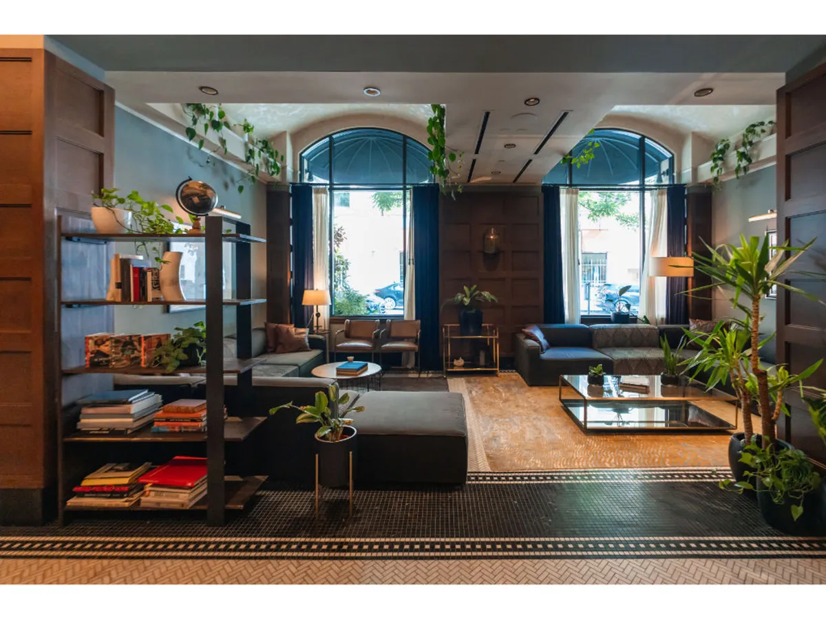 A spacious, light-filled seating area with comfortable chairs, large windows, shelves lined with books and decorative plants, and a chic coffee table—perfect for relaxing, socializing, or enjoying a welcome beverage.