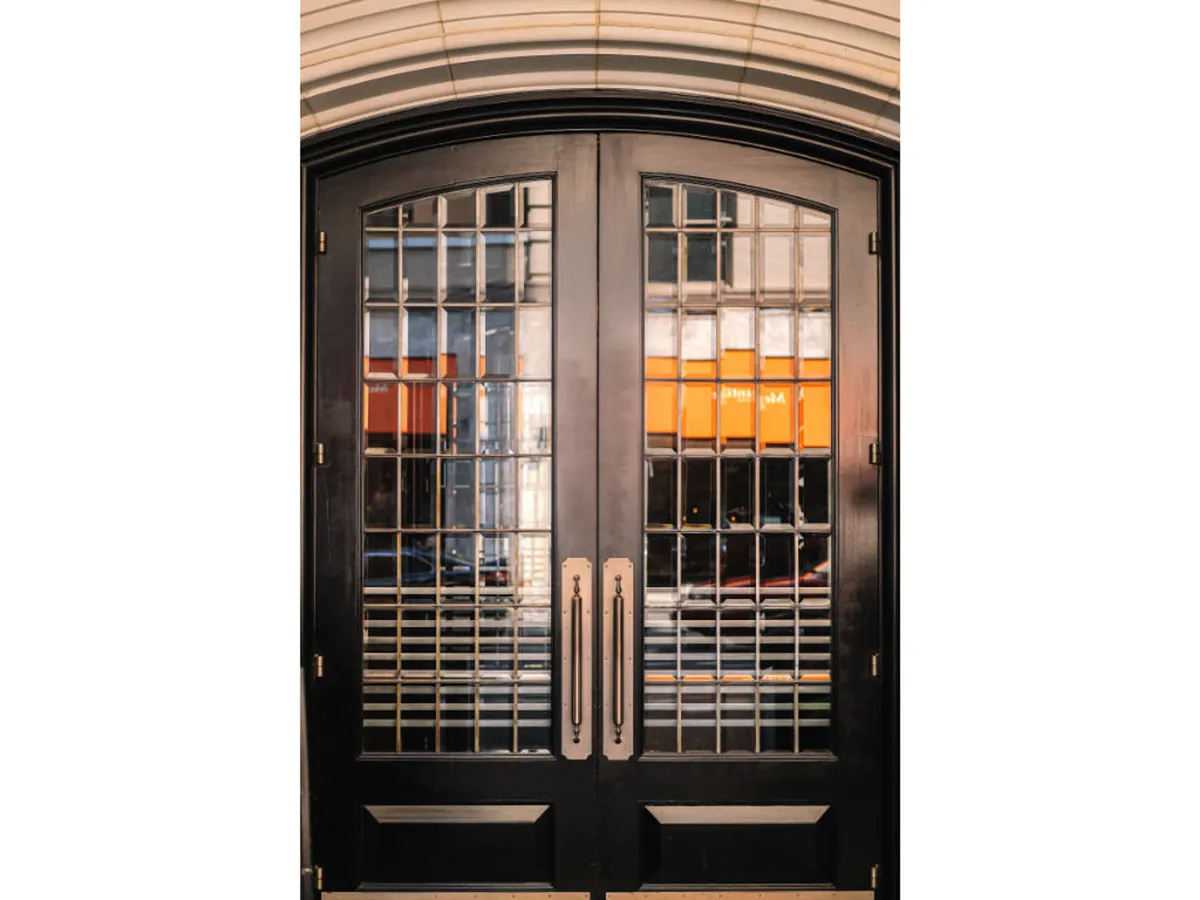 This image highlights the ornate double doors with intricate glass design and brass handles, suggesting a transition from the city outside to the sophisticated interior. The doors are slightly ajar, inviting guests to step inside and start their curated Portland adventure.