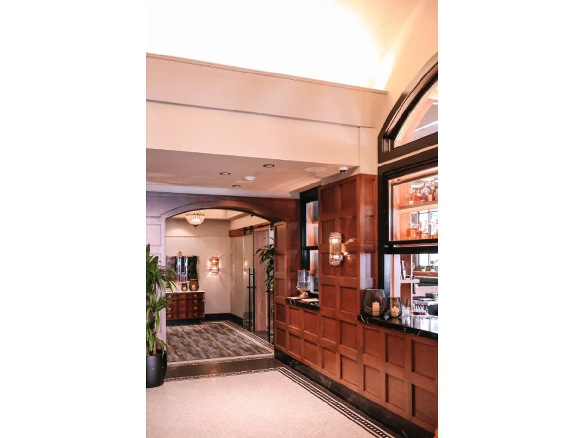 A cozy bar area with rich wood paneling, a chandelier, a green plant, and a welcoming vibe, ideal for relaxing or socializing after a day out.